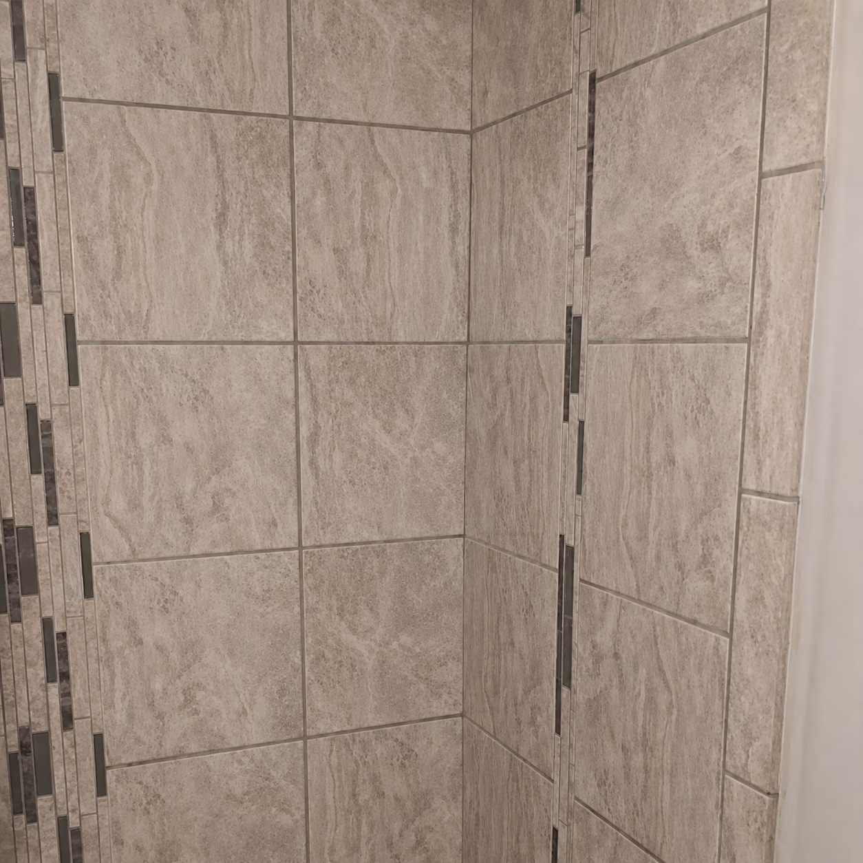 Corner wall with beige stone tiles accented by vertical strips of smaller dark mosaic tiles.