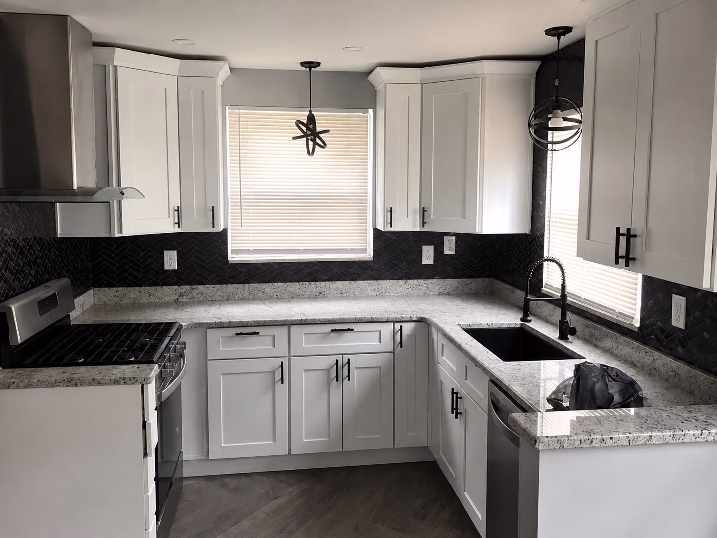 Modern kitchen with white cabinets, granite countertops, black backsplash, and stainless steel appliances.