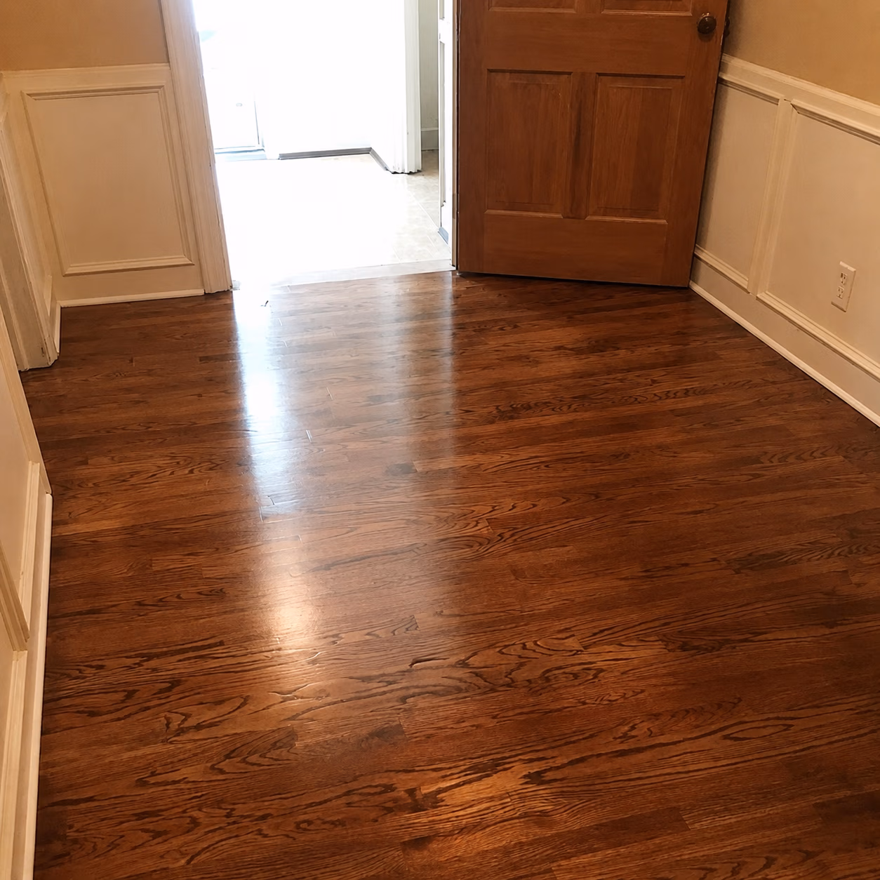 Polished hardwood floor with natural wood grain in a room with beige walls and a wooden door.