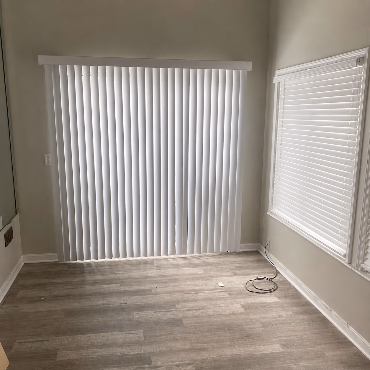 Empty room with light wood floors, white walls, vertical blinds, and a window with horizontal blinds.