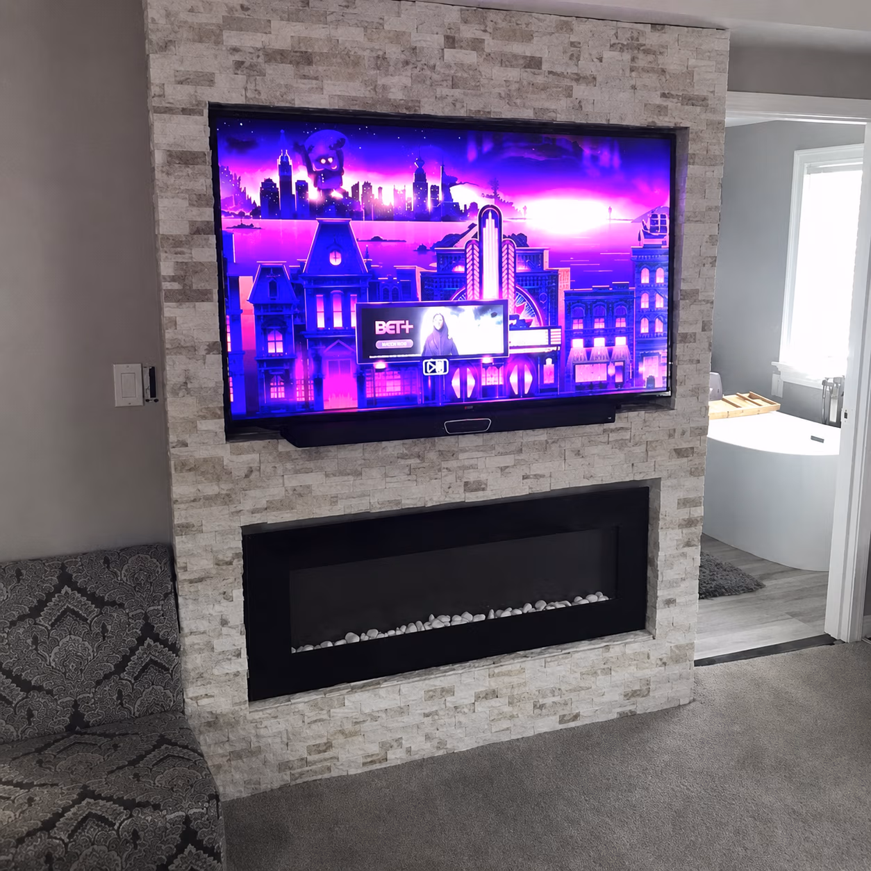 Modern living room with mounted TV showing purple cityscape and black electric fireplace below.