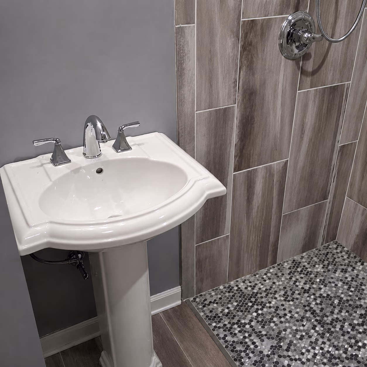 White pedestal sink with chrome faucet next to a tiled shower with pebble mosaic floor.