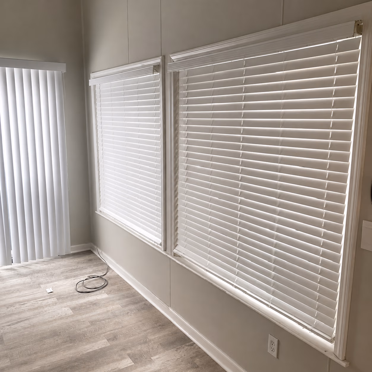 Room corner with two windows covered by white horizontal blinds and vertical blinds on a sliding door.