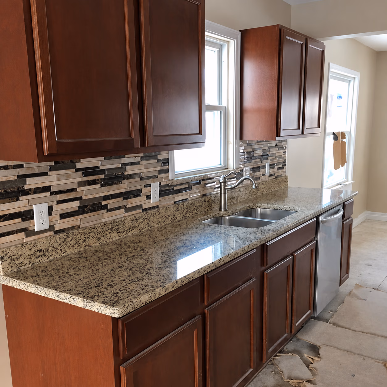 Kitchen with granite countertop, double sink, tiled backsplash, wood cabinets, and uninstalled flooring.