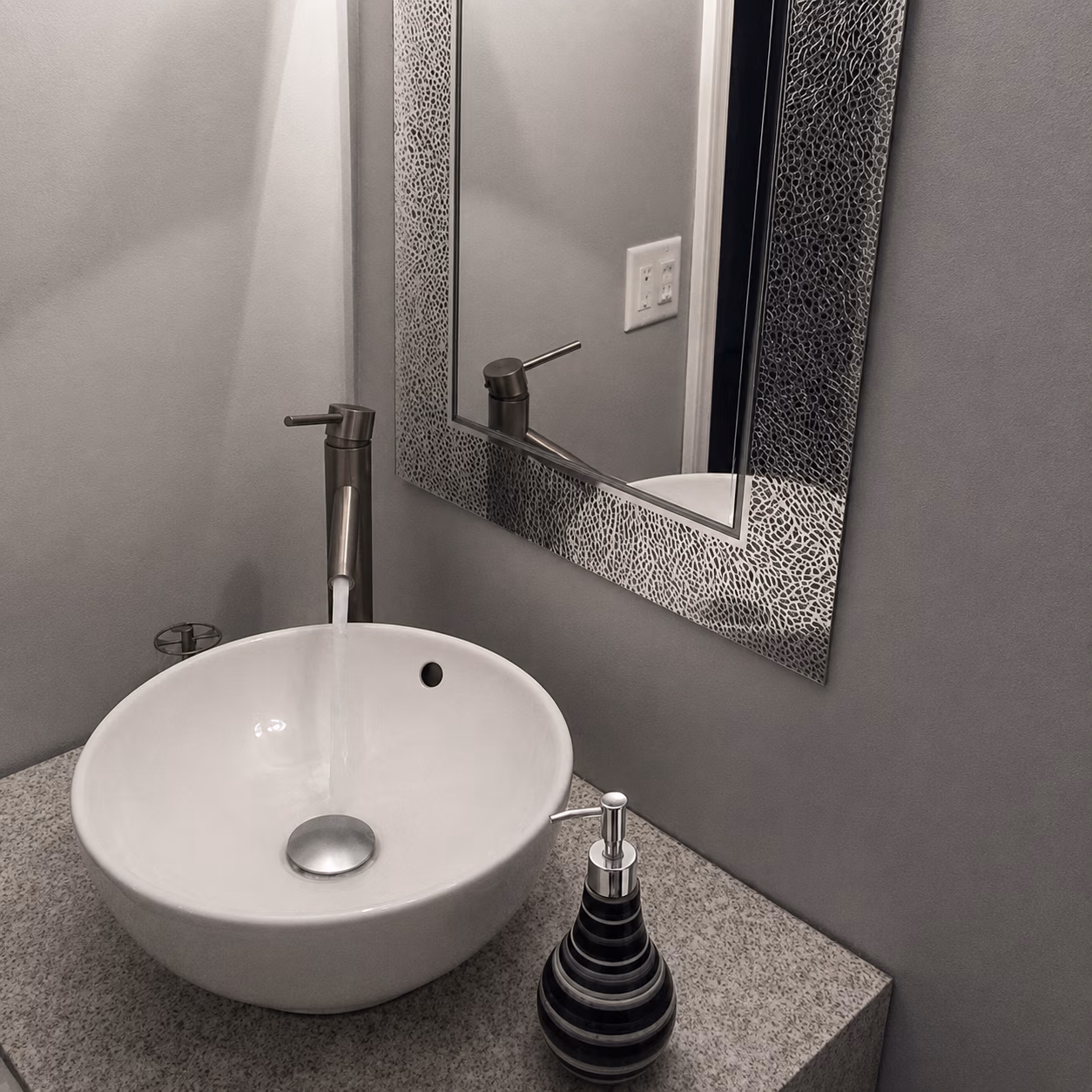 Modern bathroom sink with running faucet, round white basin, soap dispenser, and textured rectangular mirror.