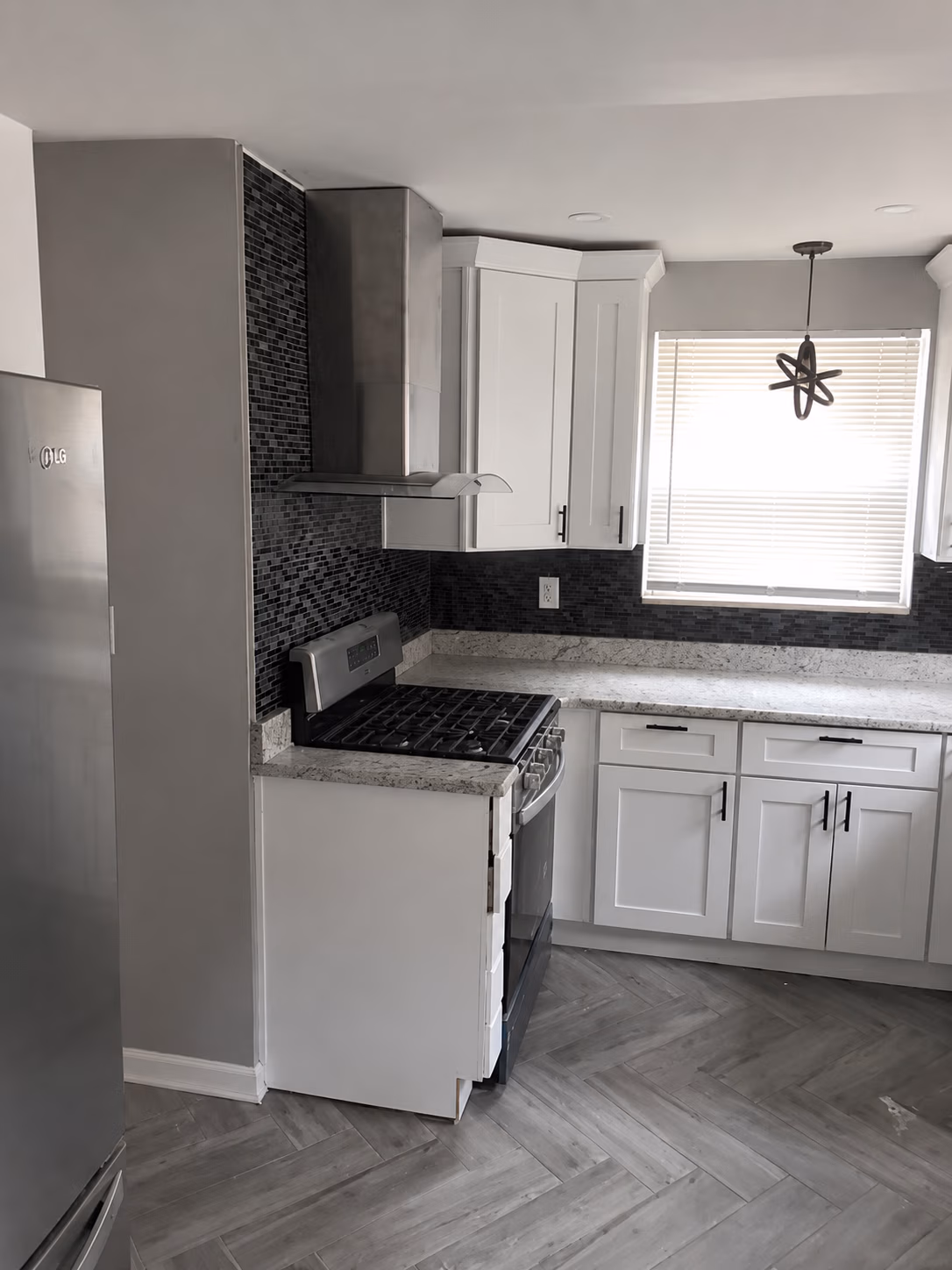Modern kitchen with stainless steel stove, white cabinets, gray tile backsplash, and window with blinds.
