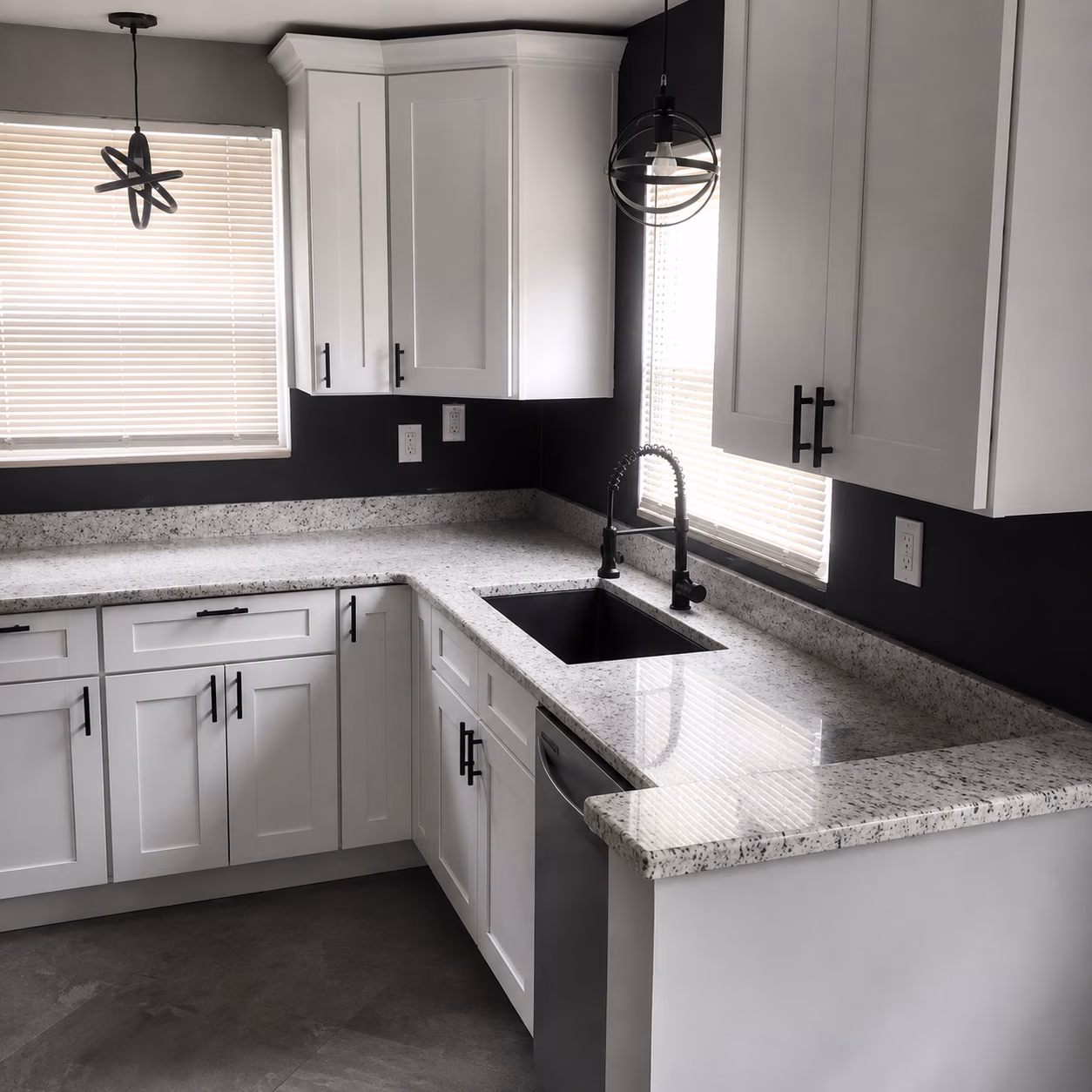 Modern kitchen with white cabinets, black faucet, granite countertops, and two pendant lights over windows.