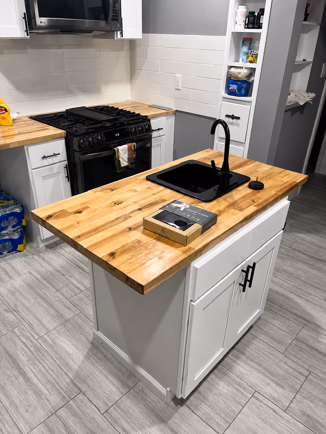 Modern kitchen with wooden countertops, black sink and faucet, black stove, white cabinets, and tiled floor.