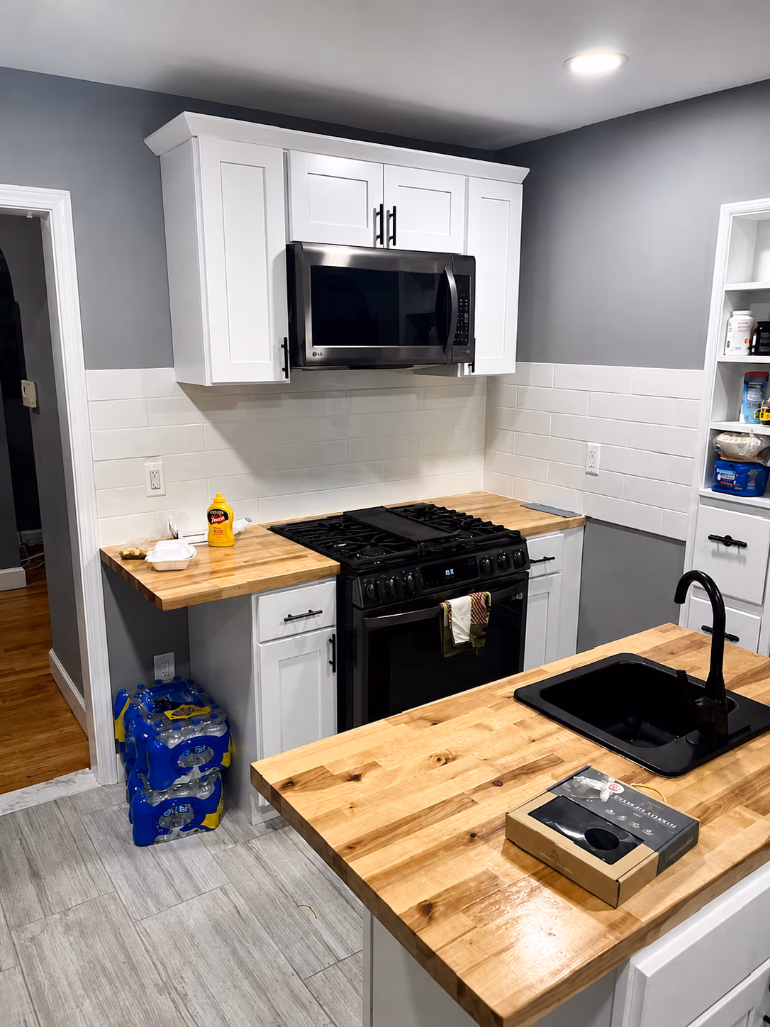 Modern kitchen with white cabinets, black stove and microwave, wood countertops, and black sink faucet.